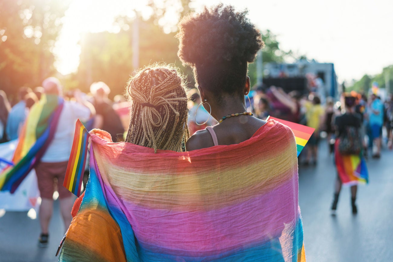 1155237469 Rear view image of young couple walking with the pride event, hugging and waving pride flags