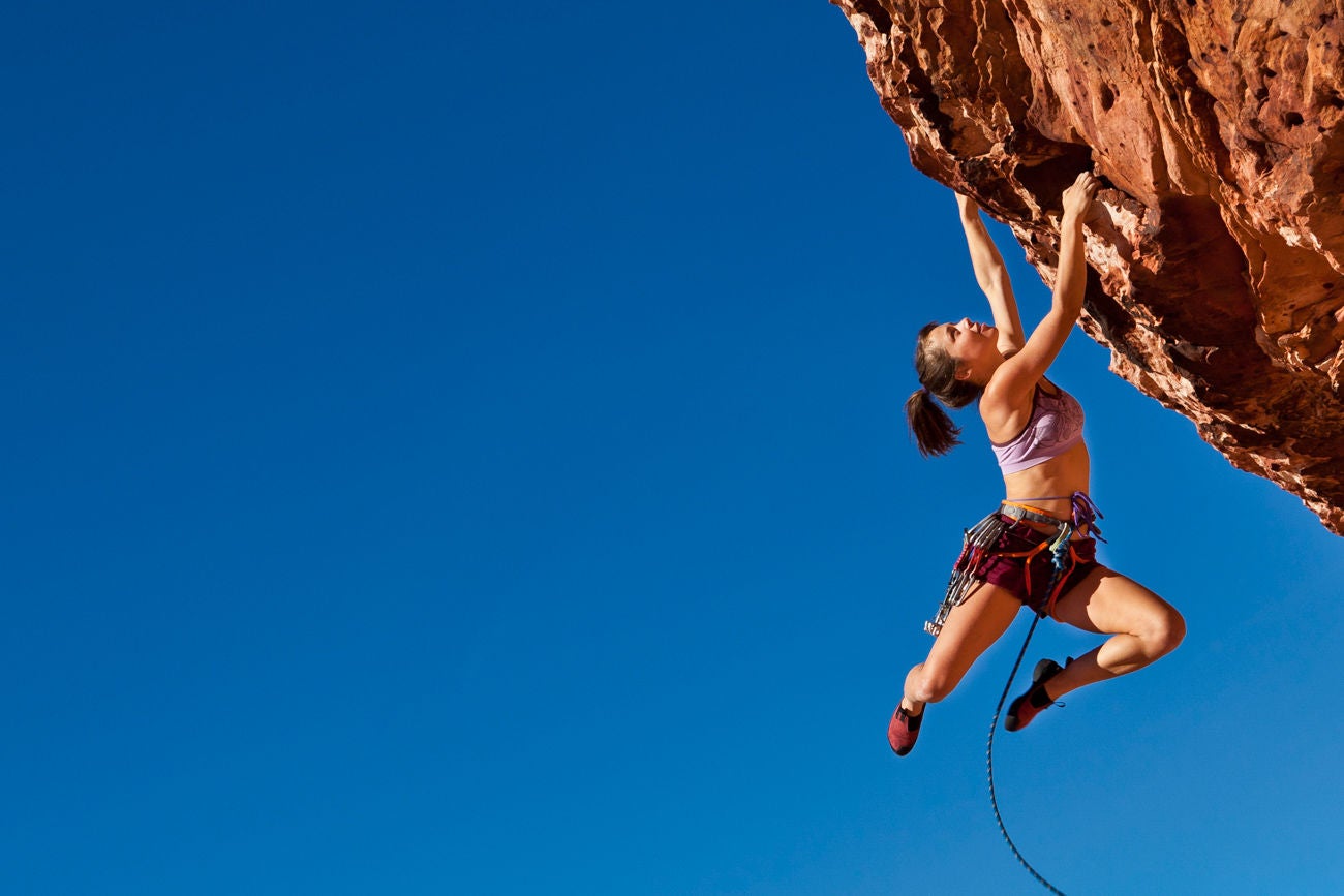 Female rock climber struggles up a cliff for her next grip on a challenging ascent.