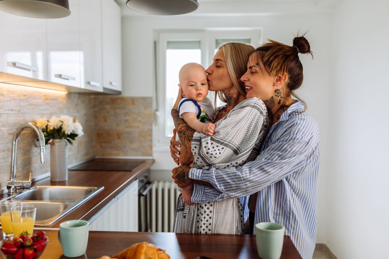 1323929771 Same sex couple in pajamas hold their baby son and enjoying time spent together at home