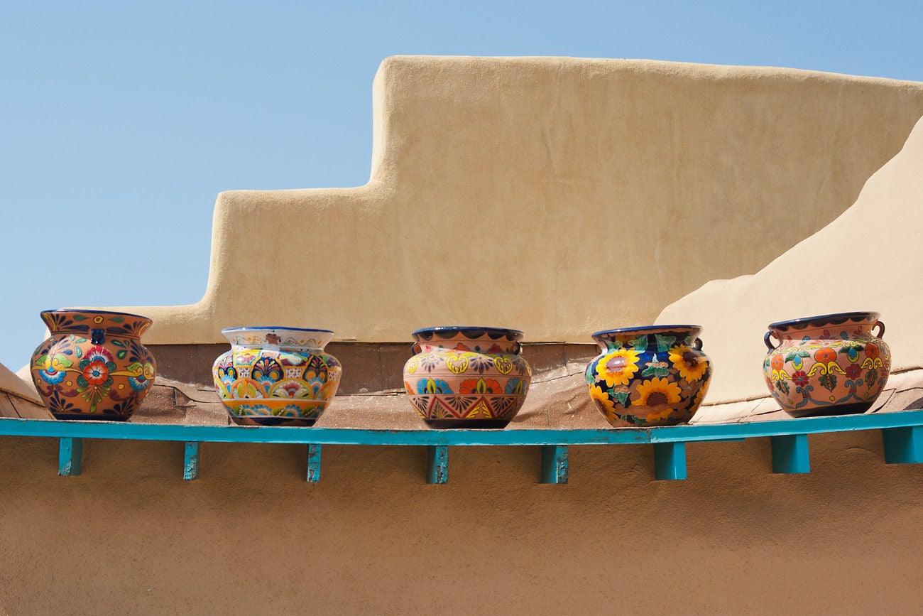 "Five empty but colorful pots sit on an old slumping ledge on the roof of an adobe pueblo building in Taos, New Mexico.  There is plenty of copy space available."