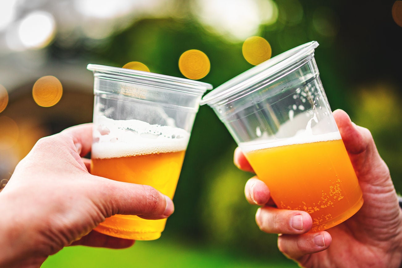 two plastick glass of beer in hand. Beer clinking outdoor