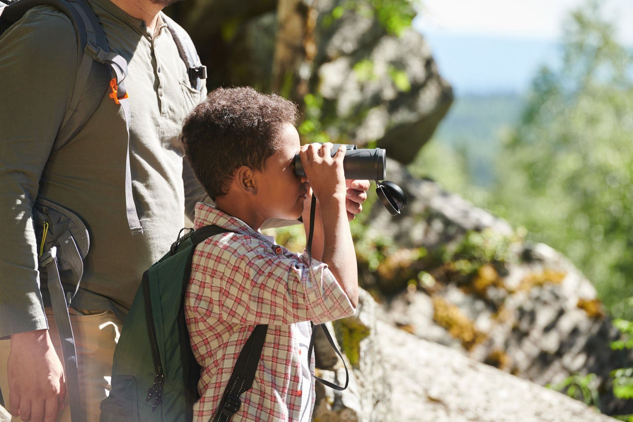 African little boy looking through the binoculars while standing in the nature together with the man