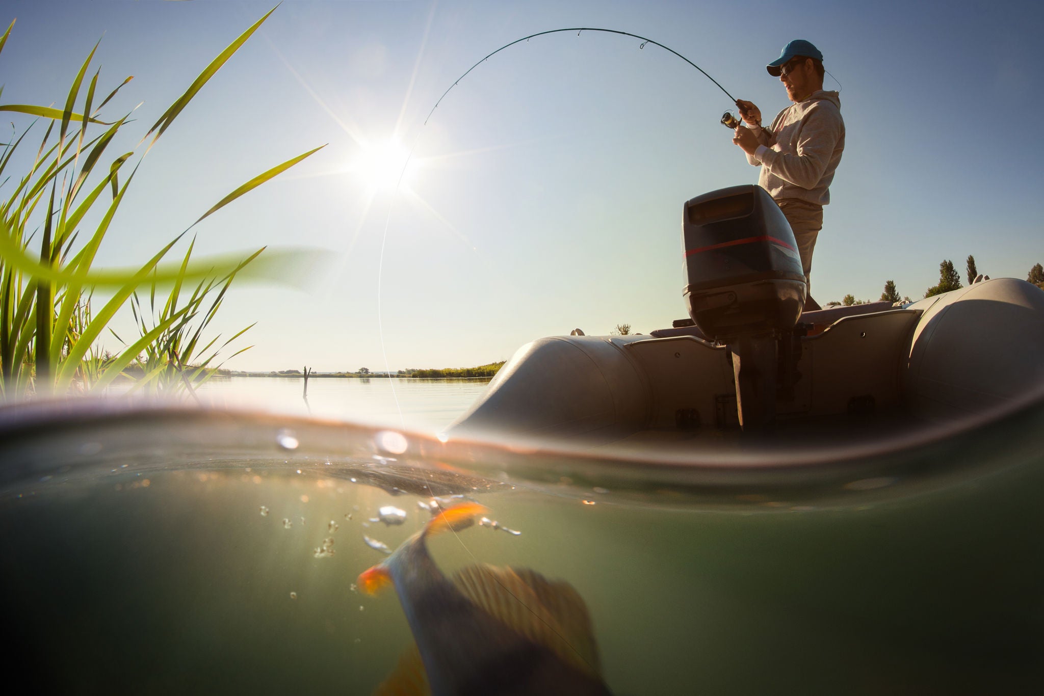 Wide shot of man reeling in his fish with the fish still visable under water.