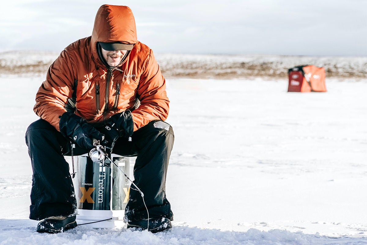 Man in orange coat ice fishing.