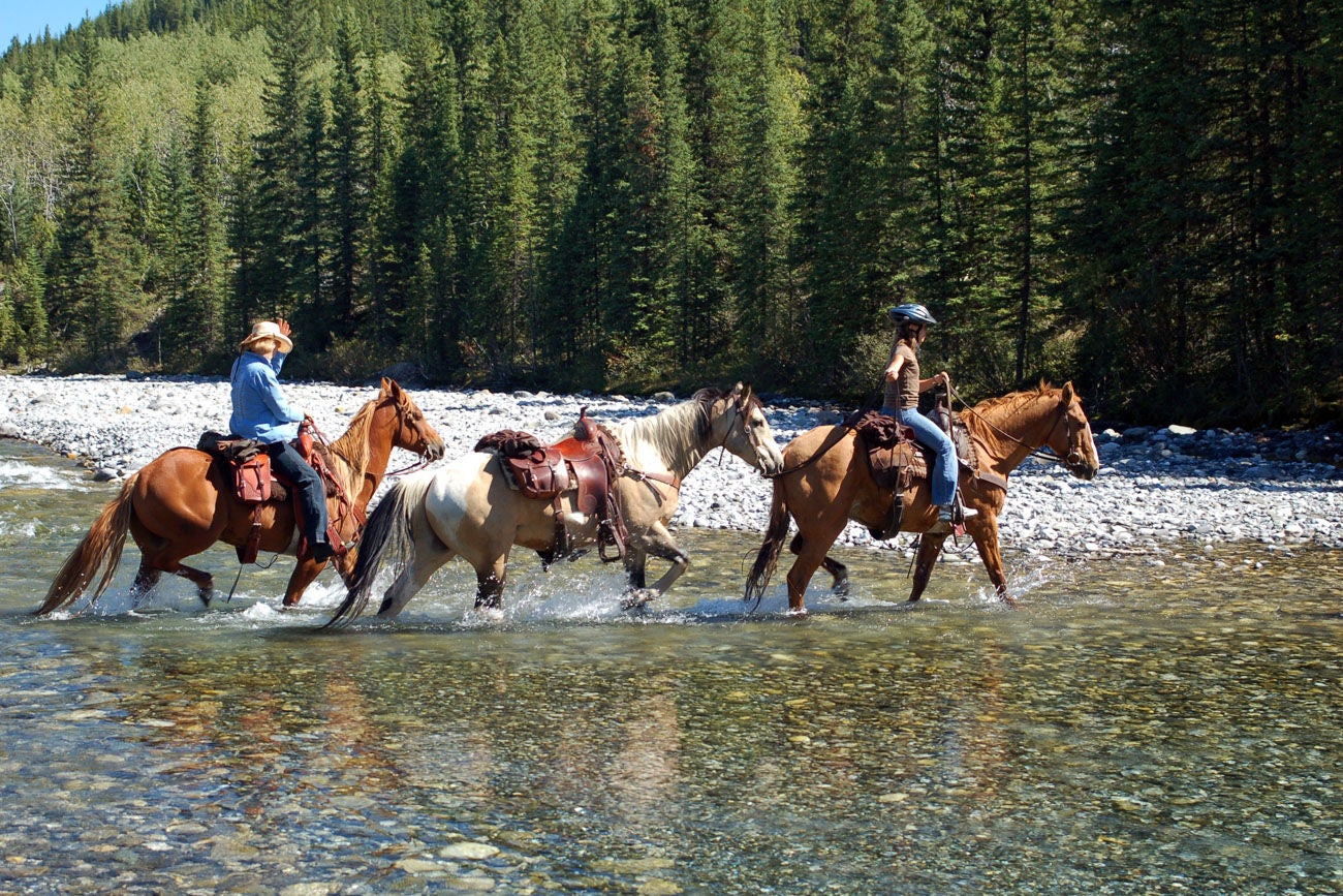 Two riders leading a riderless horse across a river in the Rocky Mountains