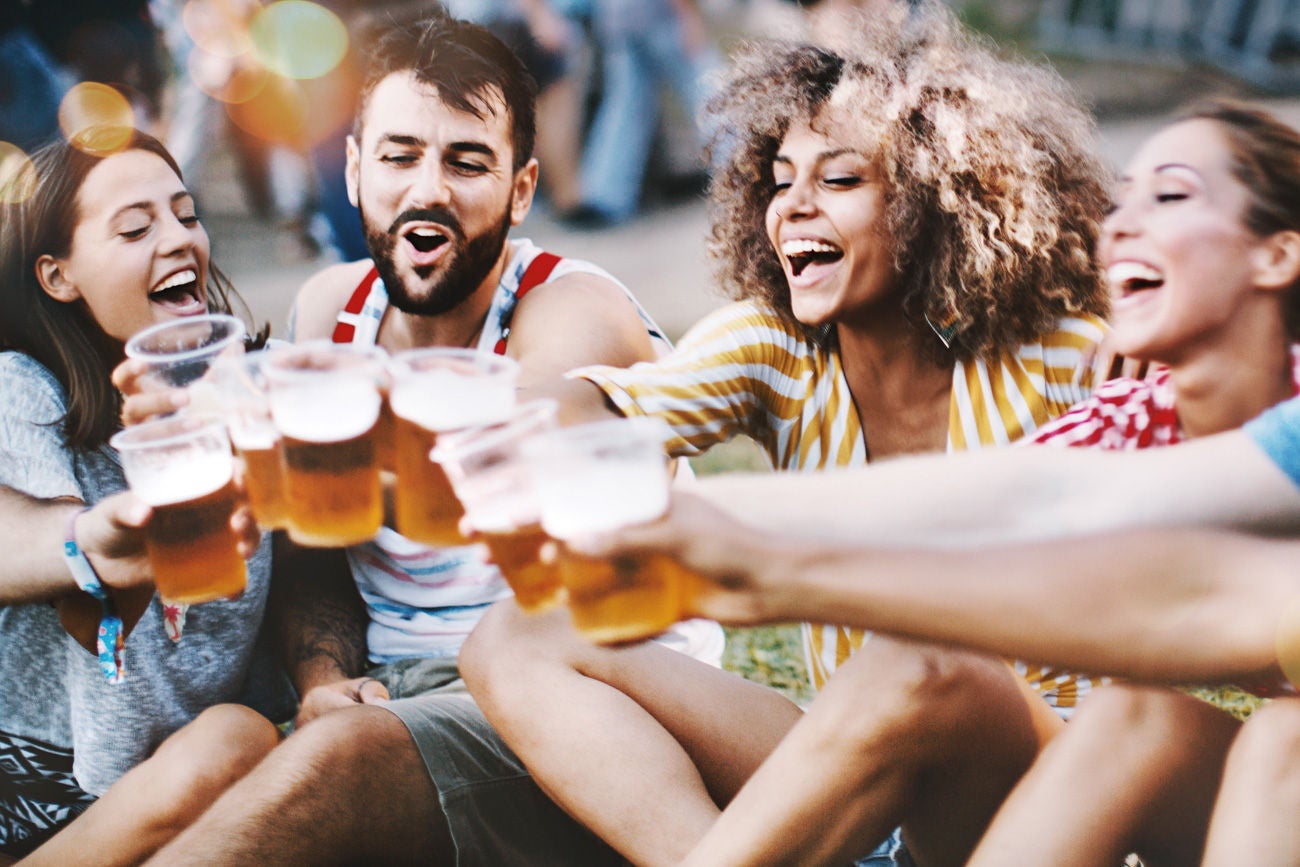 Closeup of group of young adults having some beers while hanging out on a summer afternoon. One of them is partially visible but released.