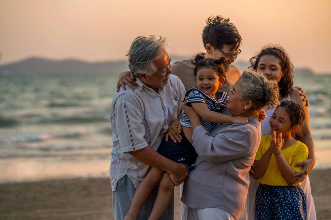 Happy big Asian family on beach holiday vacation. Multi-generation family holding hands and walking together on tropical beach at summer sunset. Family enjoy and having fun outdoor activity lifestyle.